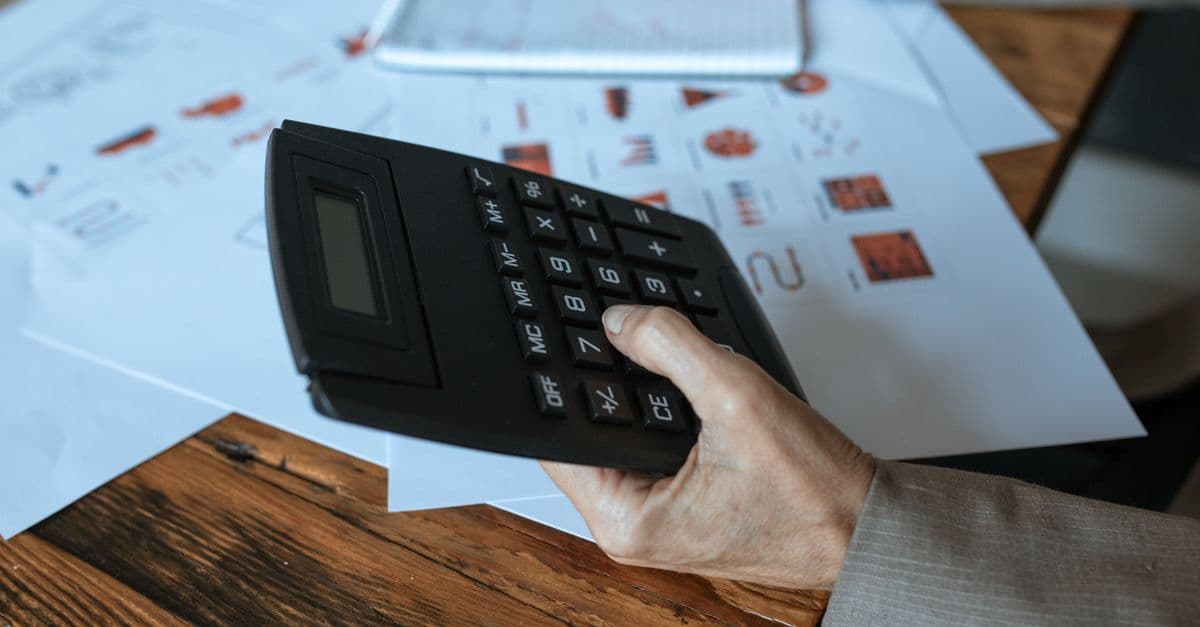 A hand using a calculator over printed charts and financial paperwork