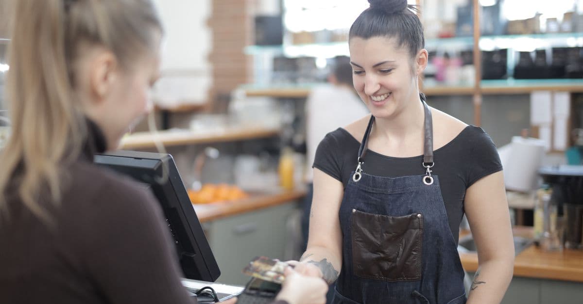 A smiling cashier taking a card payment from a customer at a cafe counter