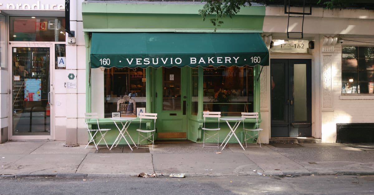 The green-awninged storefront of Vesuvio Bakery, with sidewalk cafe tables out front