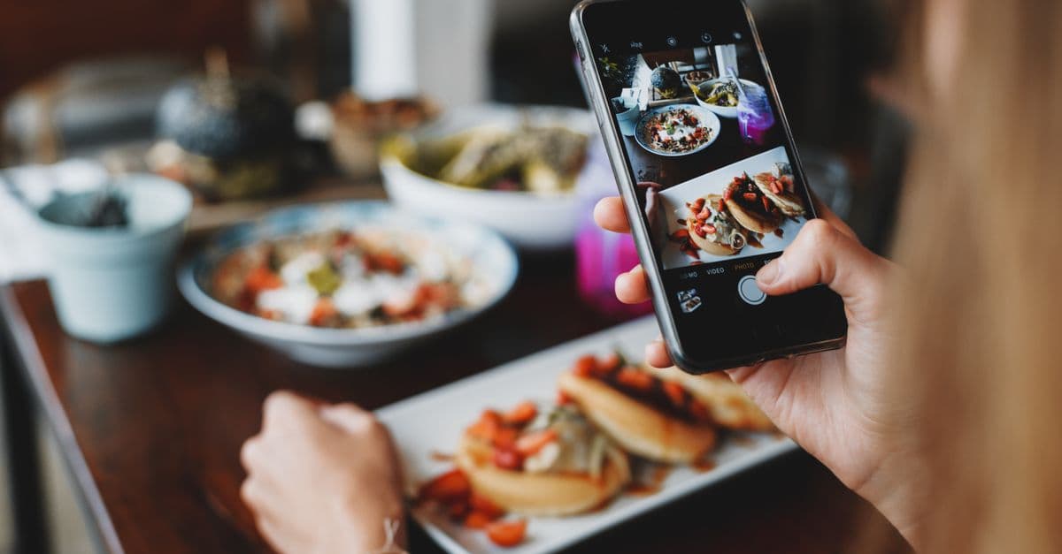 A person photographing a plated dish with a smartphone at a restaurant table