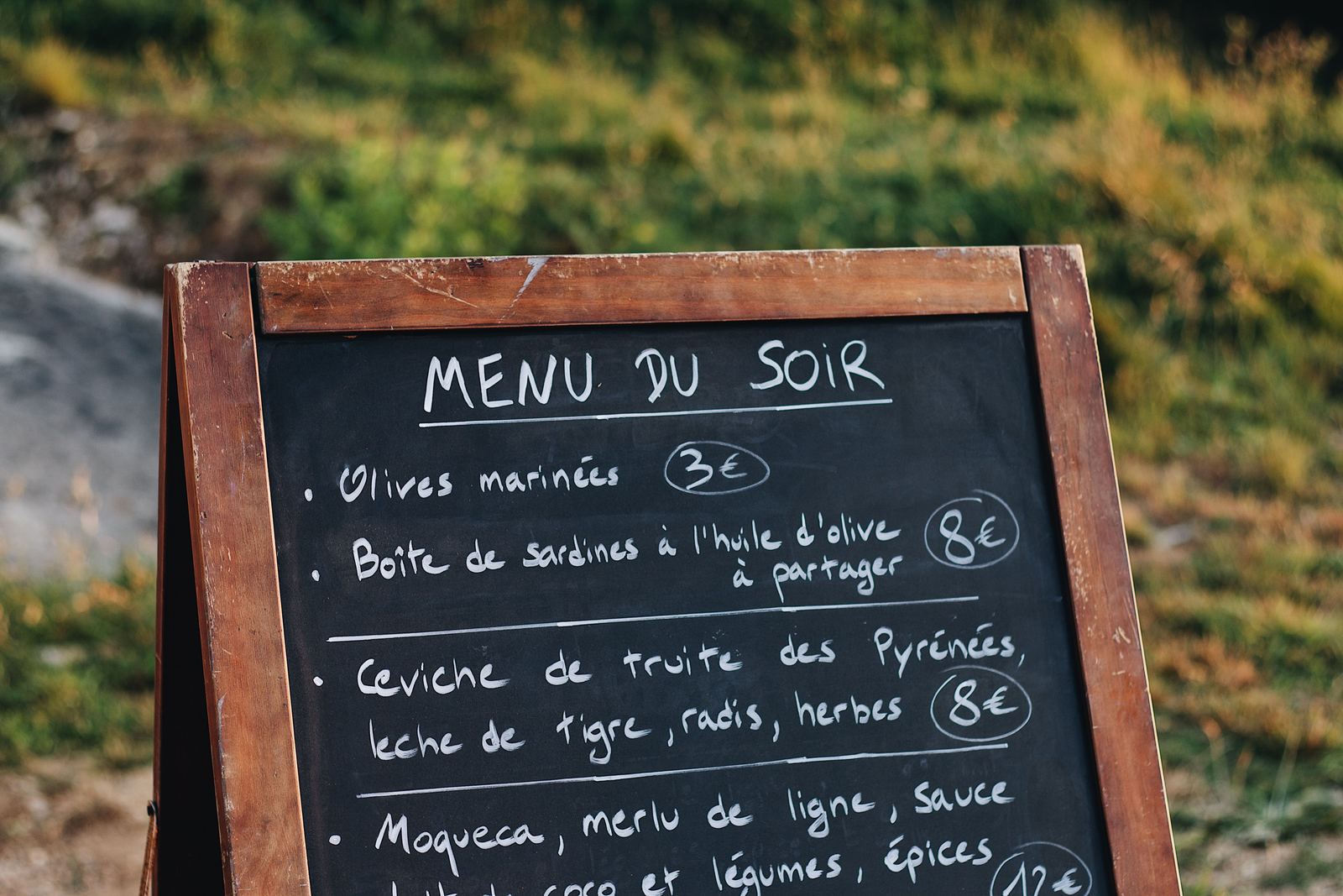 Chalkboard menu stand listing French dishes and prices in an outdoor setting