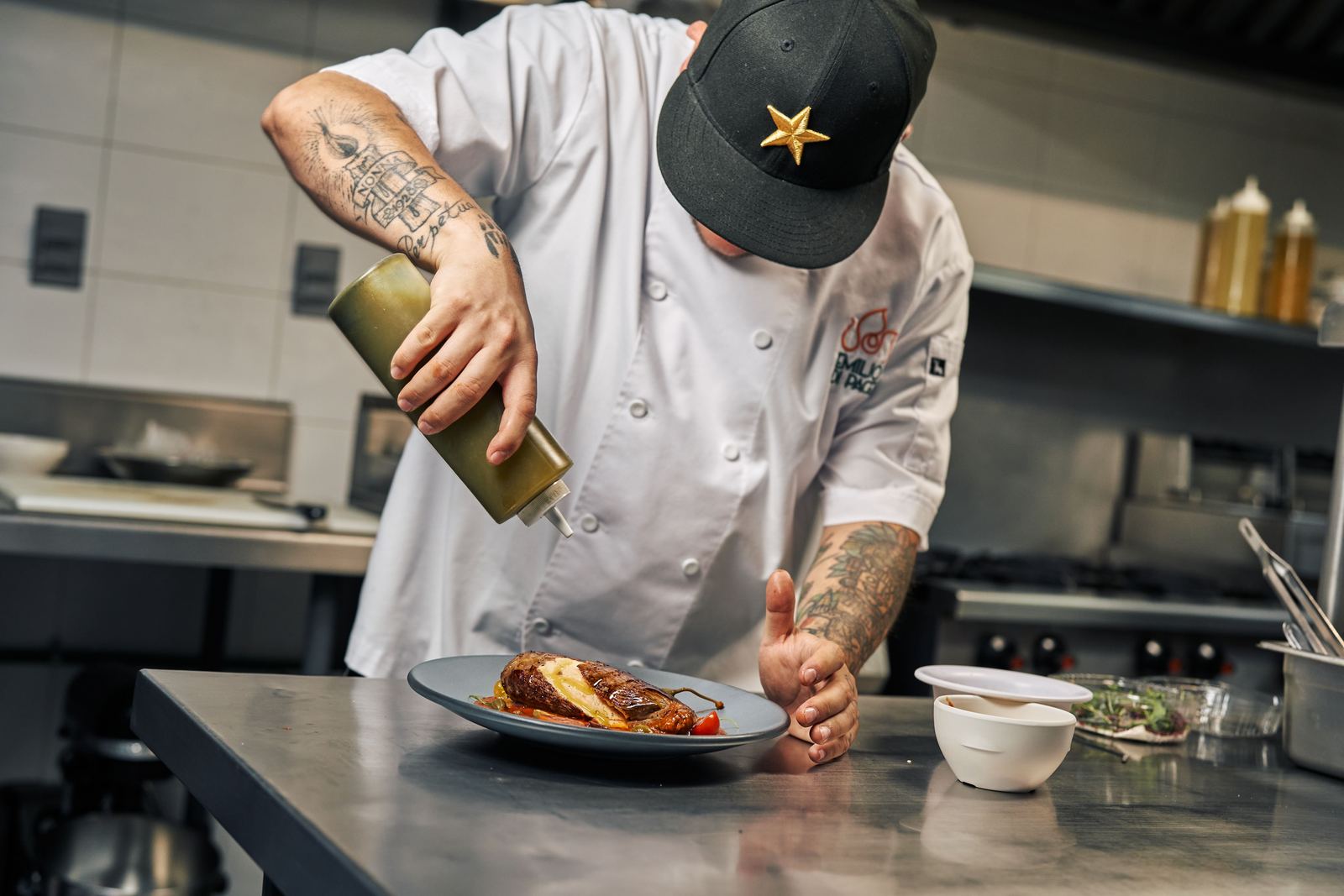 Chef garnishing a gourmet dish with sauce in a professional kitchen setting