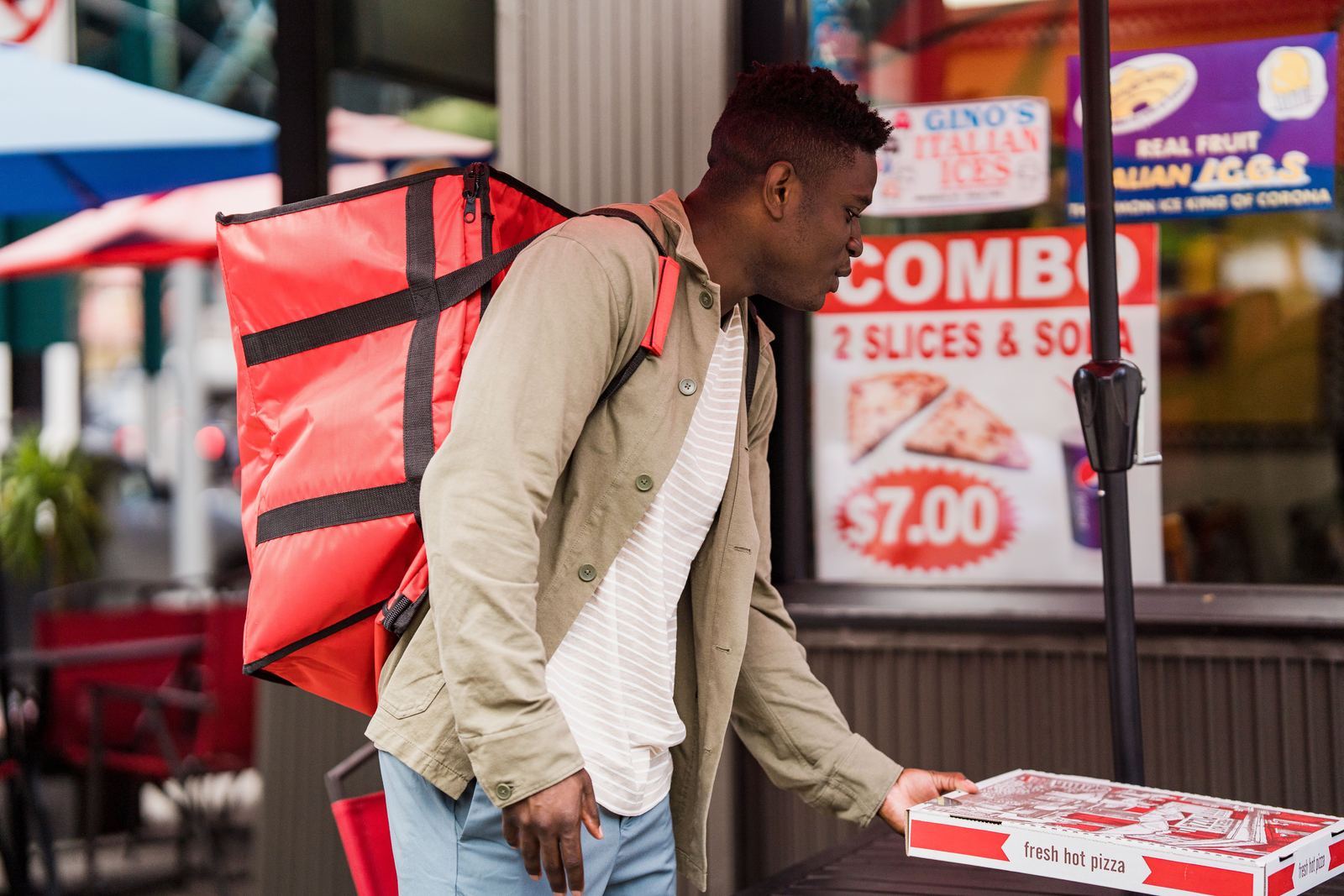 A delivery courier with an insulated bag collecting a pizza order from a restaurant